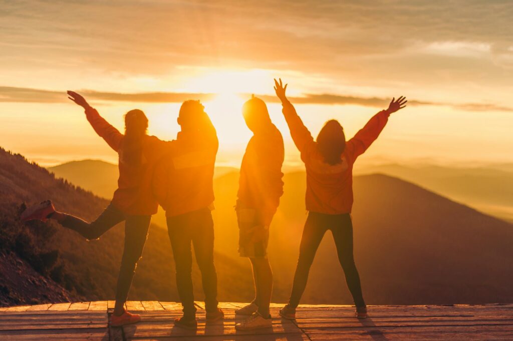 Silhouetted group of adults celebrating at sunset with mountain views.
